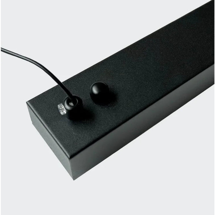 A close-up of a black electronic power cord on a linear light fixture