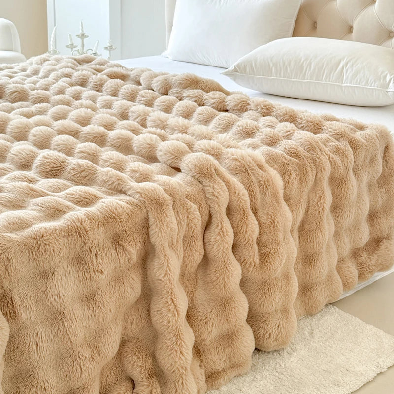 Beige fluffy blanket on a bed with white pillows and headboard.