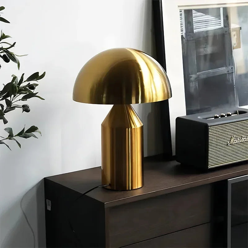 Gold table lamp on a wooden surface with a plant and vintage radio in the background