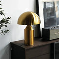 Gold table lamp on a wooden surface with a plant and vintage radio in the background