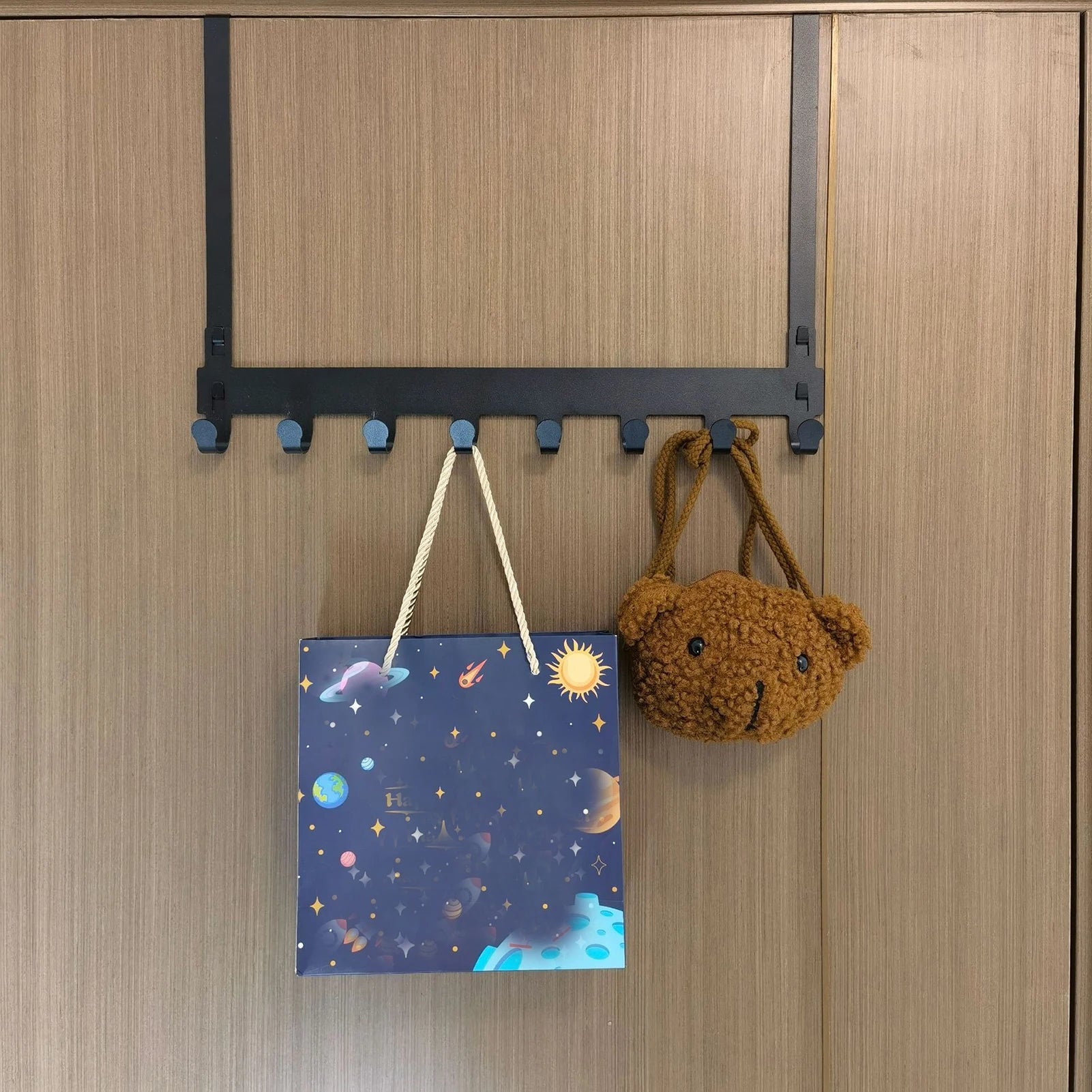 Black over-the-door organiser rack holding a coat, a handbag, and a keychain on a door