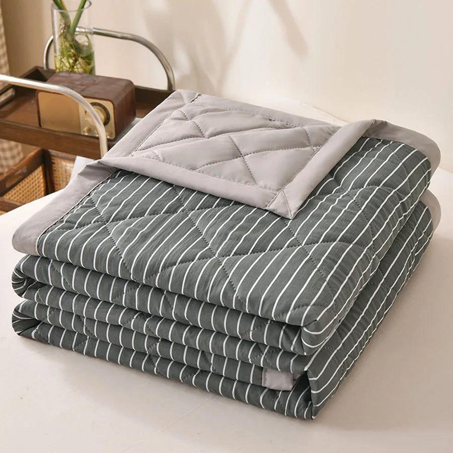 Dark grey quilted comforter with white pinstripes and a light grey border, folded on a bed