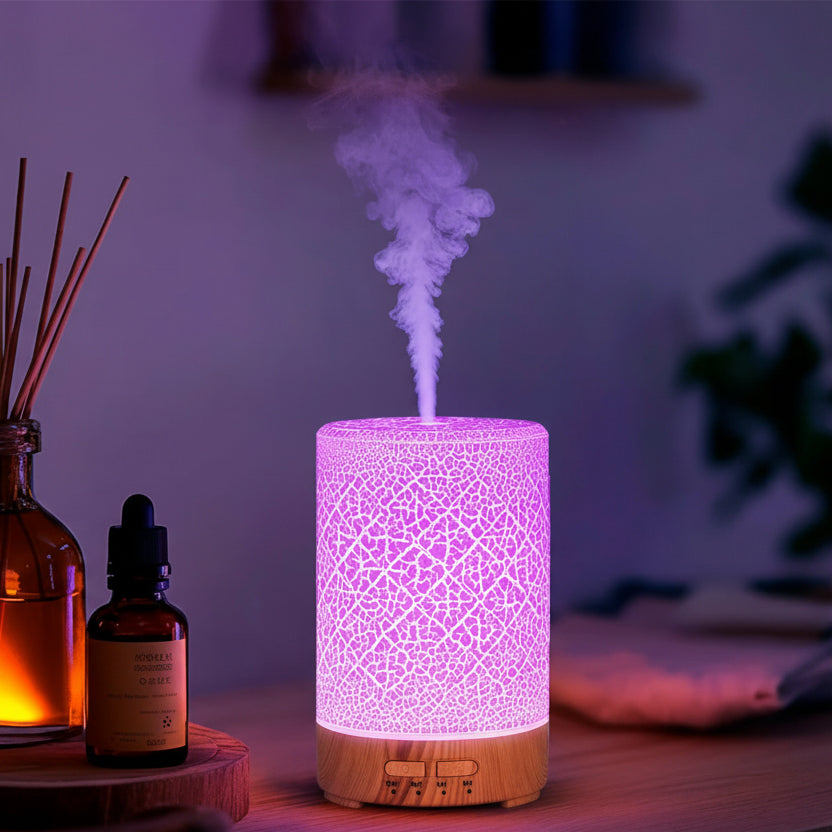 Aromatherapy diffuser emitting steam with essential oil bottles and reeds on a wooden surface.