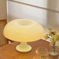 Mushroom-shaped lamp on a wooden table with a vase of flowers in the background.
