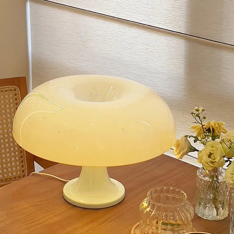 Mushroom-shaped lamp on a wooden table with a vase of flowers in the background.