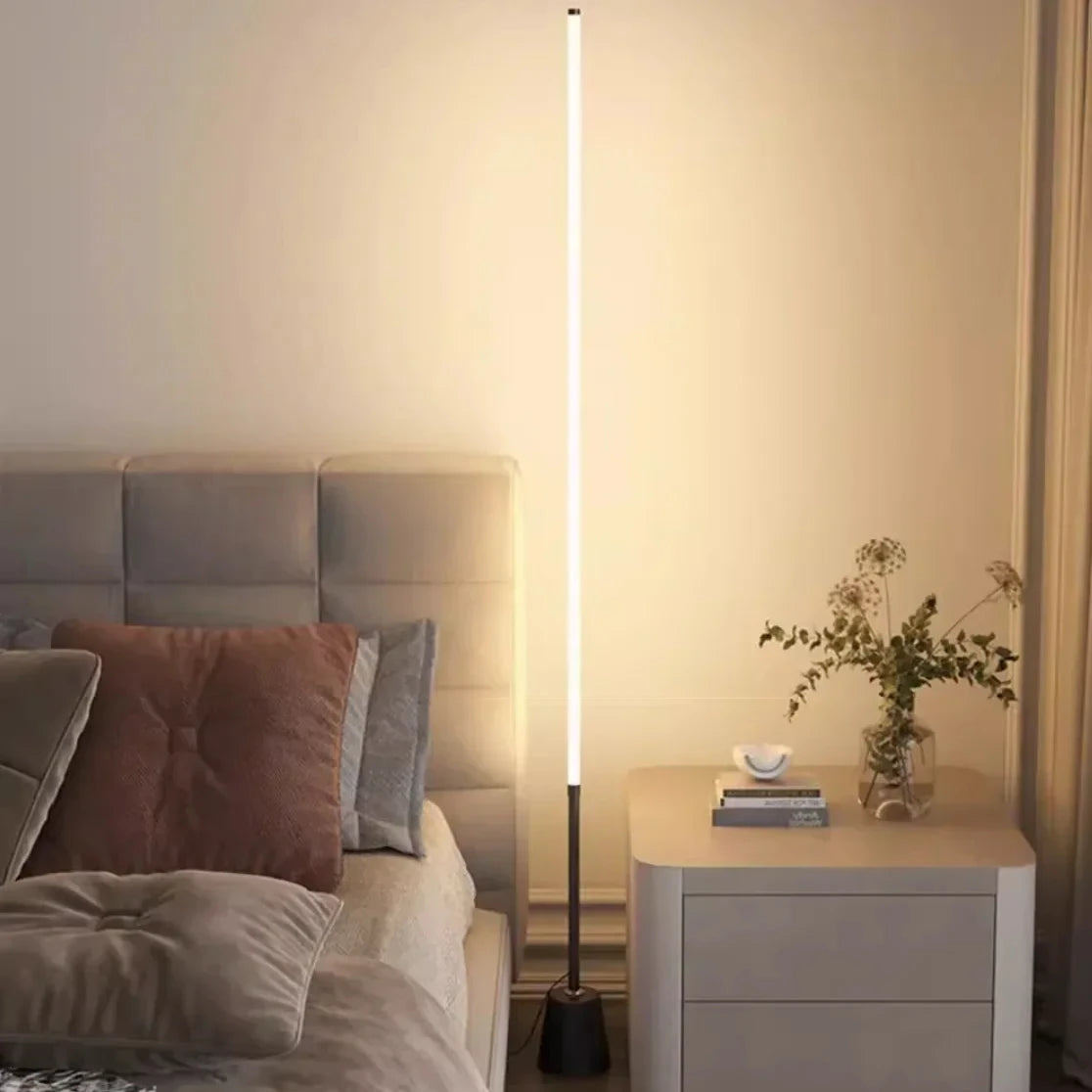 White vertical LED floor lamp beside a modern bed