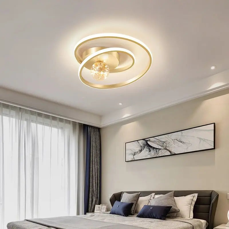 Gold Nordic spiral ceiling light with amber glass globe installed above a modern bedroom with warm ambient lighting
