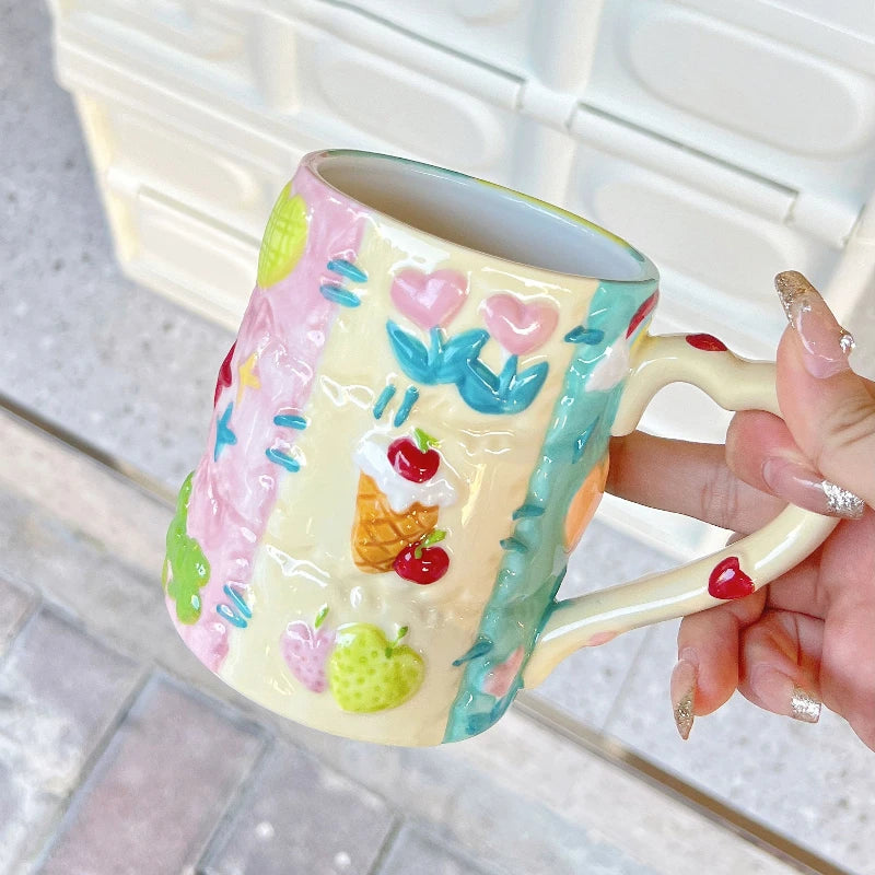 Colorful mug with floral and fruit design held by a hand.