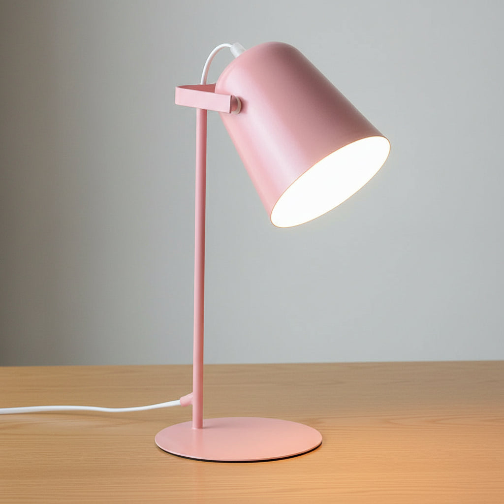 Pink desk lamp on a white surface with a vase and framed picture in the background