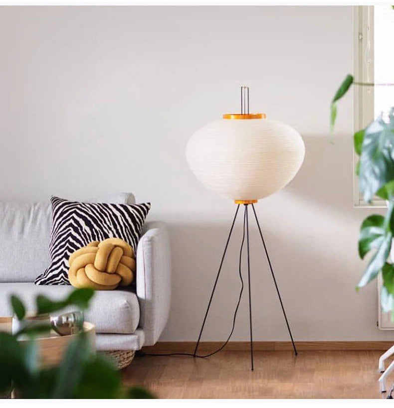 A Japanese modern floor lamp with a white shade and black legs in a living room setting.