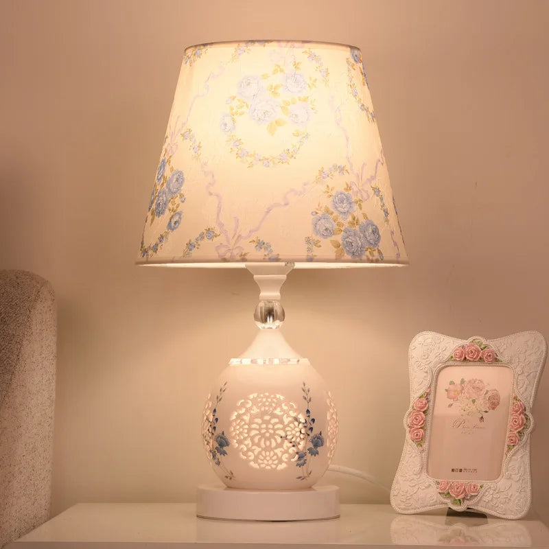 White perforated ceramic-style lamp with blue rose pattern shade near a pink rose picture frame.