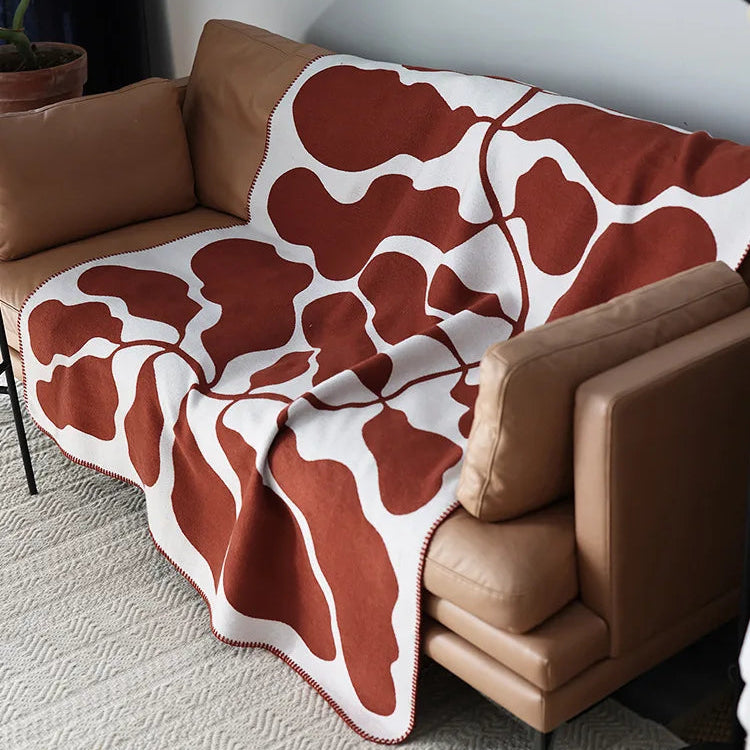 Rust and cream abstract jacquard blanket with blanket stitch edge draped over a sofa
