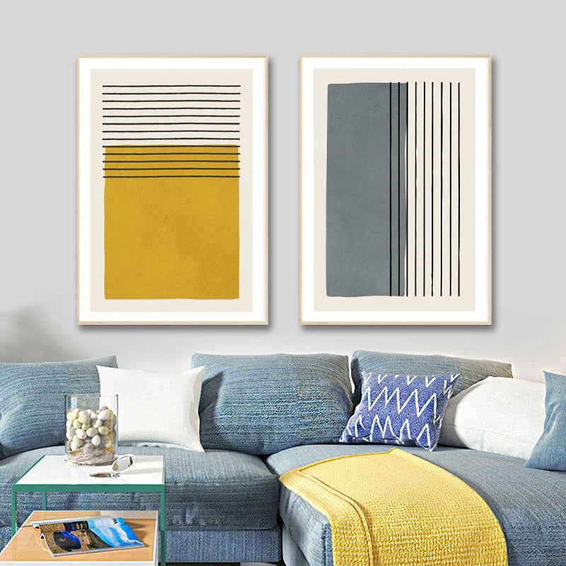 Two abstract art pieces on a wall above a blue sofa with decorative pillows and a yellow blanket.
