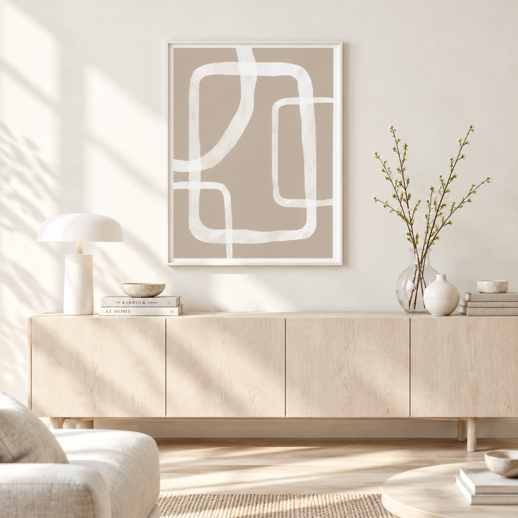 A framed abstract geometric wall art print with white curved lines on a warm beige background, displayed above a light wood sideboard in a bright, modern living room.
