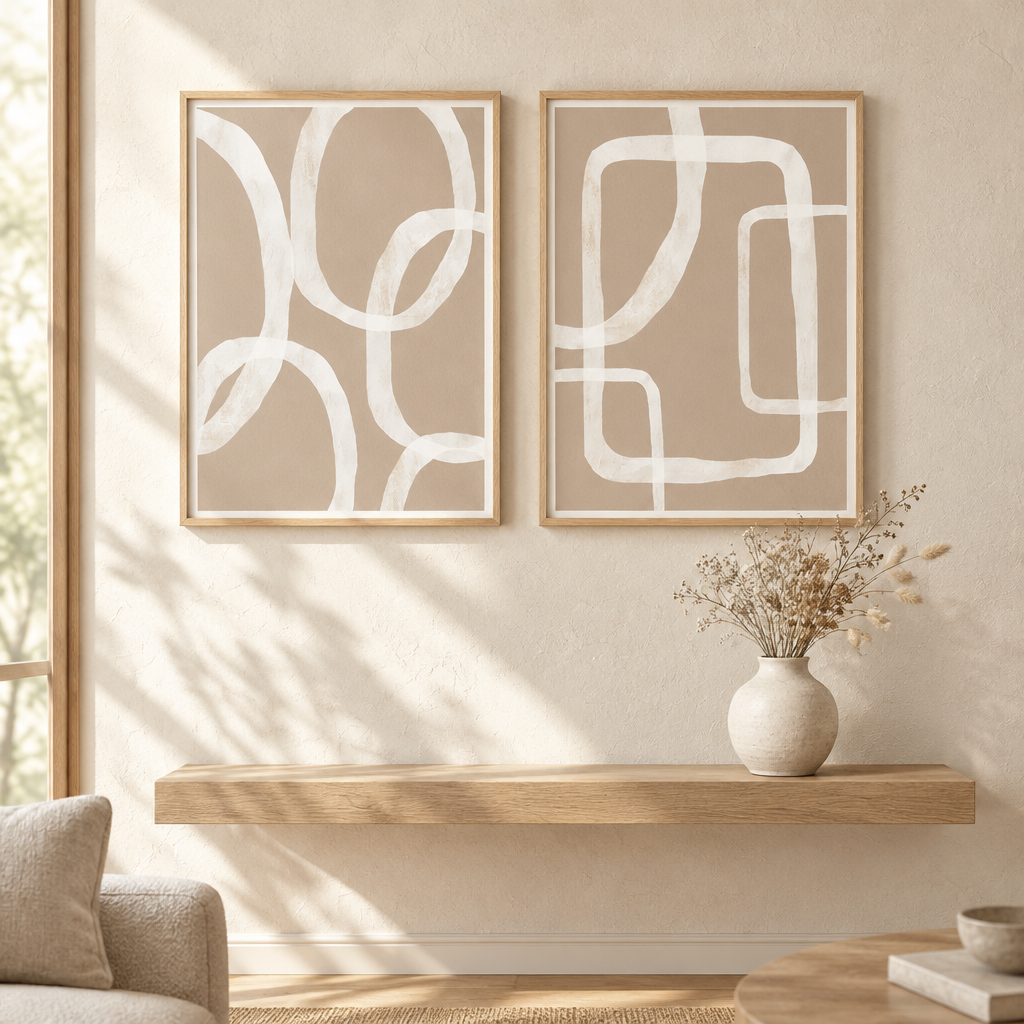 Two framed abstract wall art prints with white curved line patterns on a warm beige background, displayed above a floating wooden shelf in a softly lit living room.