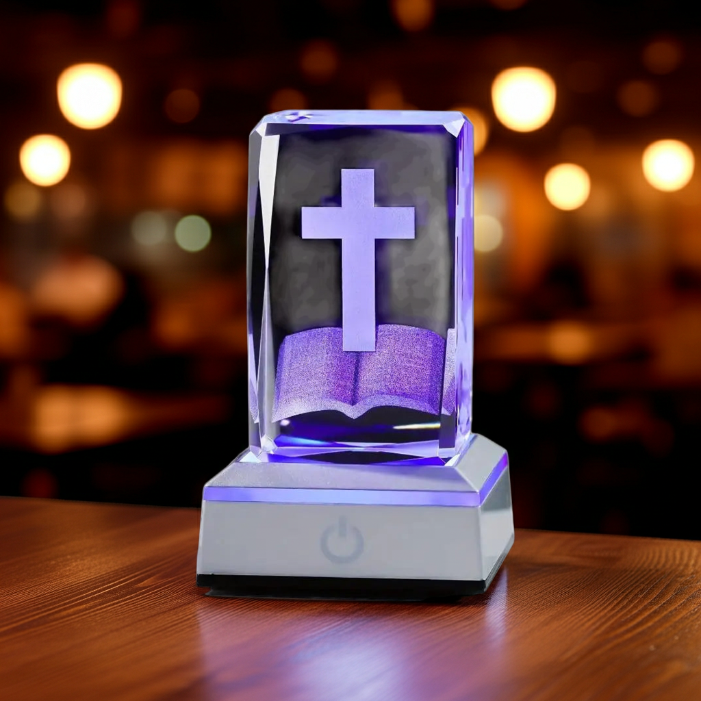 Decorative lamp with cross and book design on a wooden surface with blurred lights in the background
